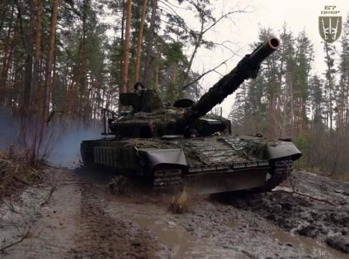 На фотографії зображено український танк Т-64БВ зразка 2022 року, який належить 67-й окремій механізованій бригаді Збройних Сил України, що рухається по багнистій лісовій дорозі