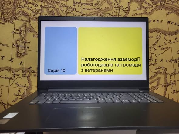 на чорному ноутбуці Lenovo, розташованому на старовинній карті, на екрані відображається презентаційний слайд українською мовою з написом «Серія 10» та темою «Налагодження взаємодії роботодавців та громади з ветеранами».