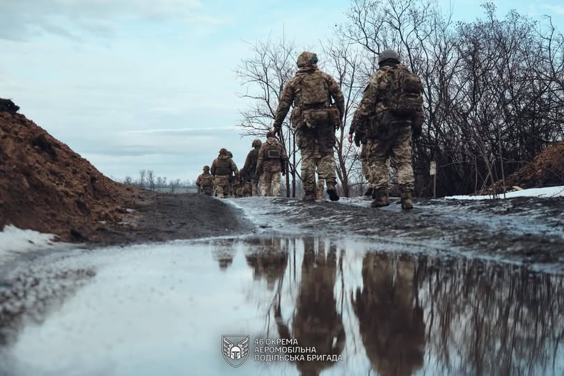 Кілька українських військовослужбовців із 46-ї окремої аеромобільної бригади йдуть по розмитій ґрунтовій дорозі з калюжами та снігом на узбіччі