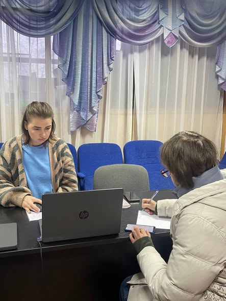 Дві людини сидять за столом в офісному приміщенні, одна працює за ноутбуком HP, а інша пише на папері