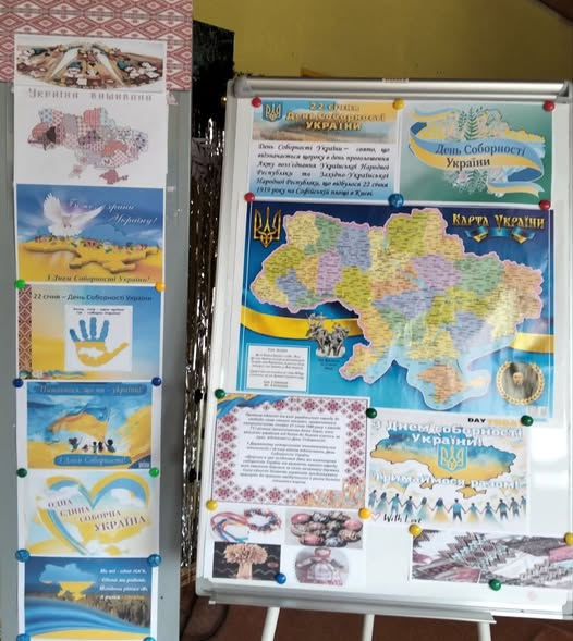 Фотографія стенду з плакатами та інформацією, присвяченими Дню Соборності України. На стенді розміщені кілька плакатів з текстами «День Соборності України» та зображеннями карти України, стилізованих людей у вишиванках, голубів миру та жовто-блакитних стрічок. Включно з великою деталізованою картою України, розфарбованою різними кольорами областей, та меншими зображеннями традиційних українських прикрас та вишивки"