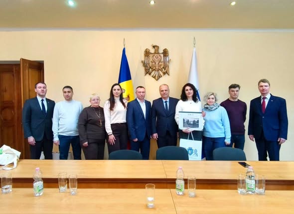 На зображенні група з десяти людей, одягнених в офіційний та напівофіційний одяг, позує для фотографії в приміщенні для засідань. На задньому плані видно прапор та герб Республіки Молдова. Люди стоять за дерев'яним столом, а двоє в центрі тримають аркуш паперу або сертифікат