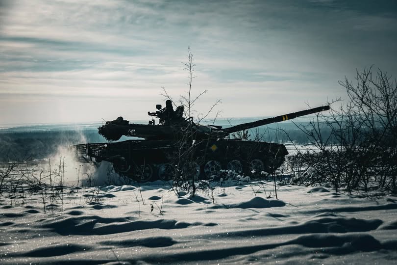 На зображенні показано силует танка Т-72 на засніженому полі, з яскравим небом на задньому плані та сухими кущами на передньому