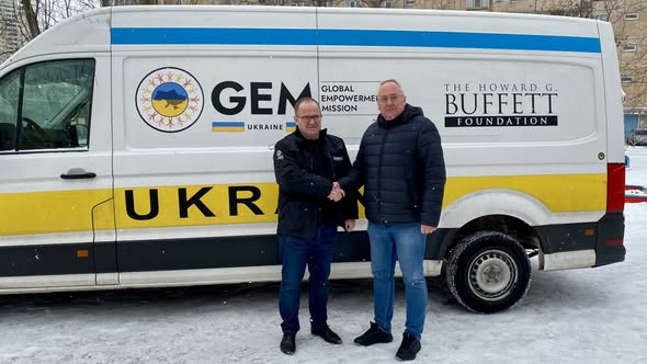 На зображенні двоє чоловіків тиснуть руки перед білим фургоном із логотипами GEM Ukraine Global Empowerment Mission та The Howard G. Buffett Foundation на сніжному тлі.