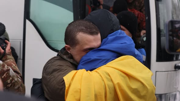 Український військовослужбовець та близька людина тепло обіймаються, причому одна особа загорнута в синьо-жовтий прапор