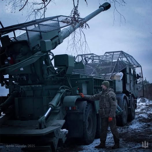 Українська 155-мм самохідна артилерійська установка 2С22 «Богдана» на бойовій позиції. Артилерист 54-ї окремої механізованої бригади стоїть поруч із установкою на засніженій місцевості.