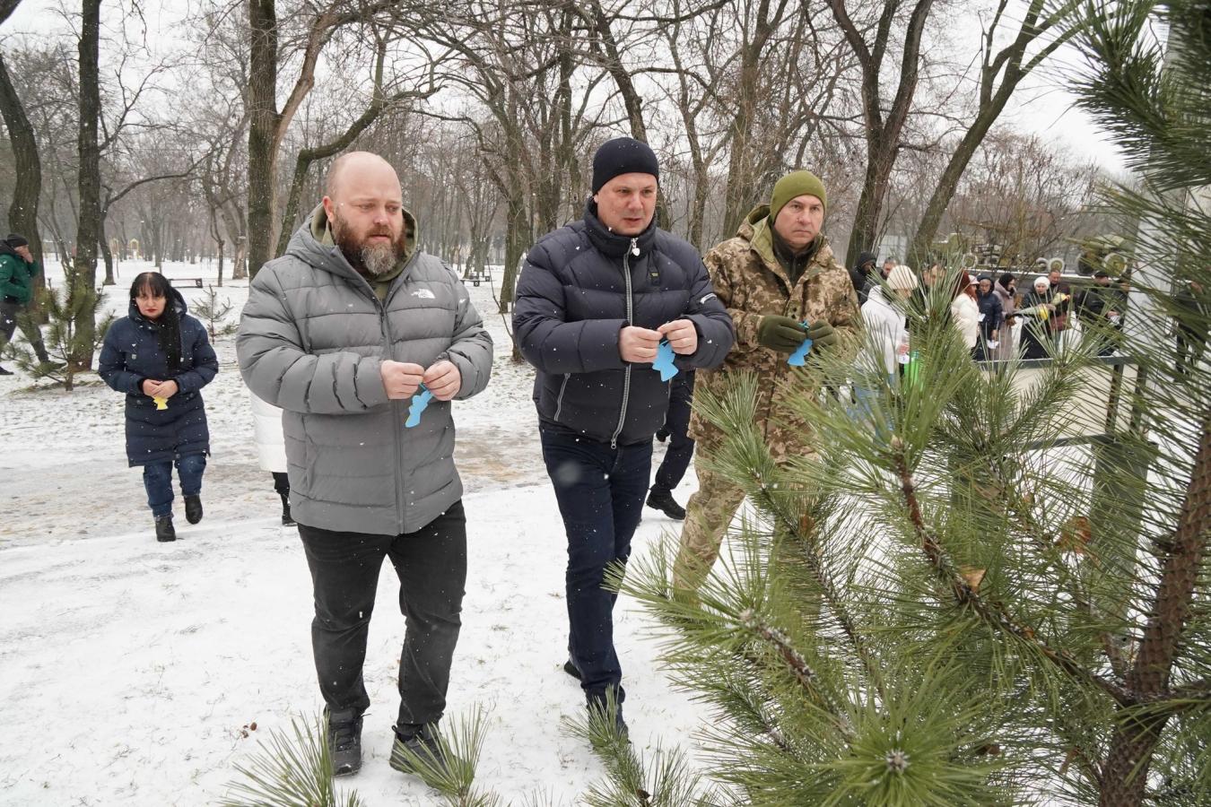 Учасники меморіальної акції в засніженому парку вішають паперових янголів на гілки сосни в пам'ять про загиблих дітей.