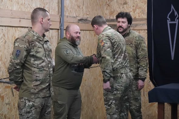 Нагородження бійців 3-ї окремої штурмової бригади. Військовий у тактичному одязі тисне руку штурмовику на фоні прапора Хорунжої служби бригади