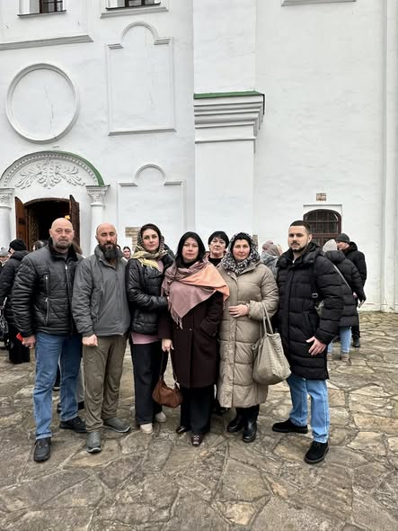 На цьому фото зафіксовано групу людей (три чоловіки та чотири жінки), які позують для спільного знімка на тлі великої білої будівлі.