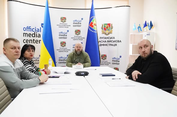 Представники Луганської обласної військової адміністрації проводять брифінг в офіційному медіацентрі на фоні державних прапорів та інформаційних стендів
