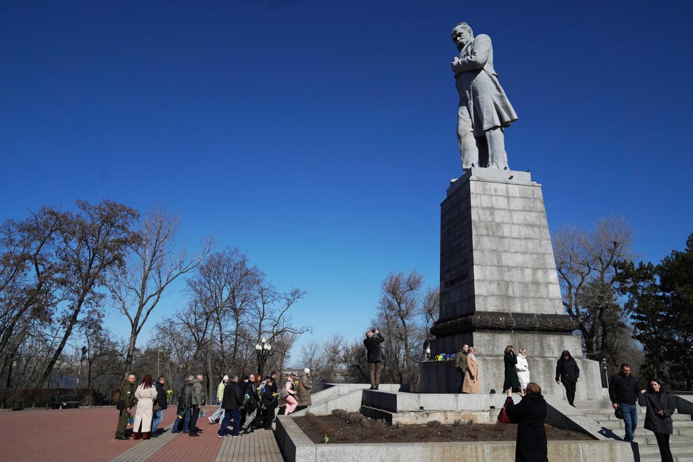 Група людей зібралася біля підніжжя високого пам’ятника Тарасу Шевченку на Монастирському острові в Дніпрі сонячного весняного дня.
