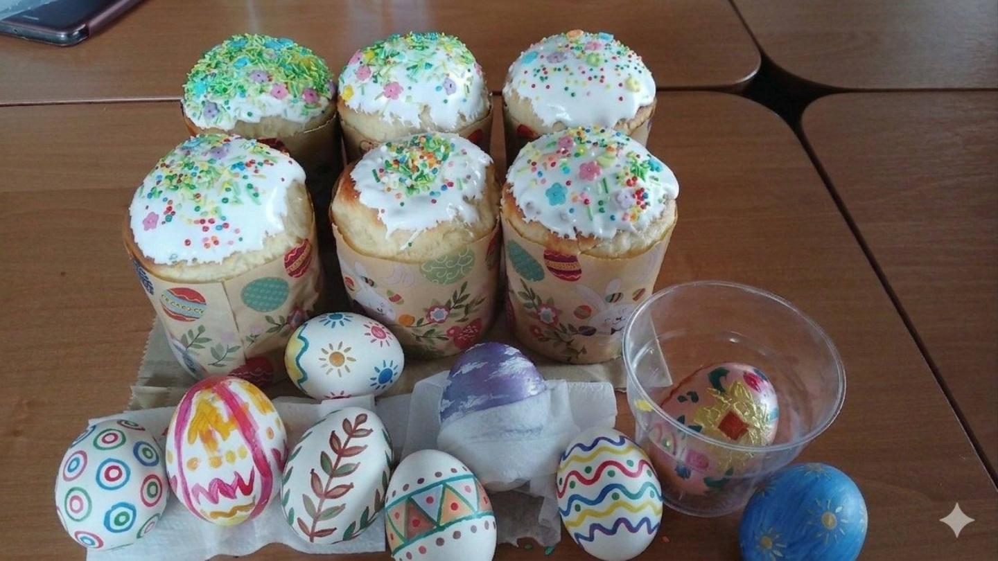 На дерев'яному столі розміщена святкова великодня композиція, що складається з шести апетитних пасок у декоративних паперових формах, покритих білою глазур'ю з різнокольоровою посипкою, та ряду власноруч розписаних писанок із різноманітними візерунками й орнаментами.