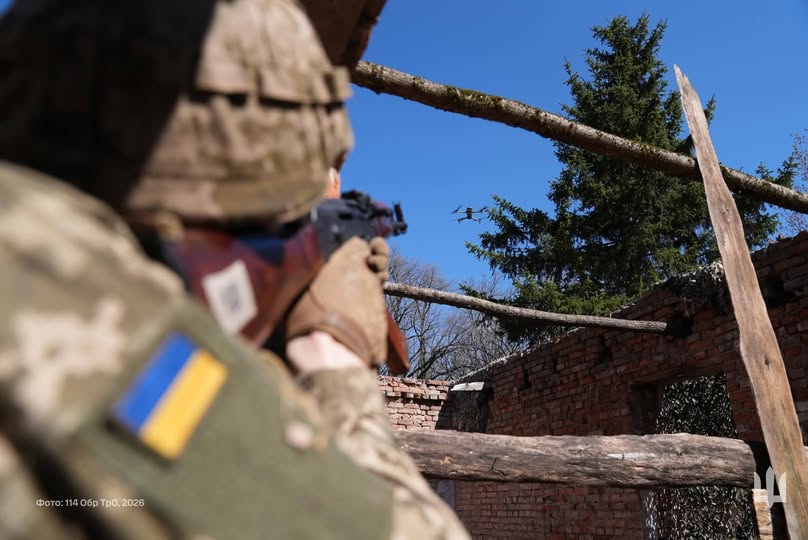 зображено українського військовослужбовця у напівпрофіль зі спини. Він перебуває всередині напівзруйнованої цегляної будівлі без даху. Солдат цілиться з автомата Калашникова у невеликий квадрокоптер, що завис у синьому безхмарному небі.