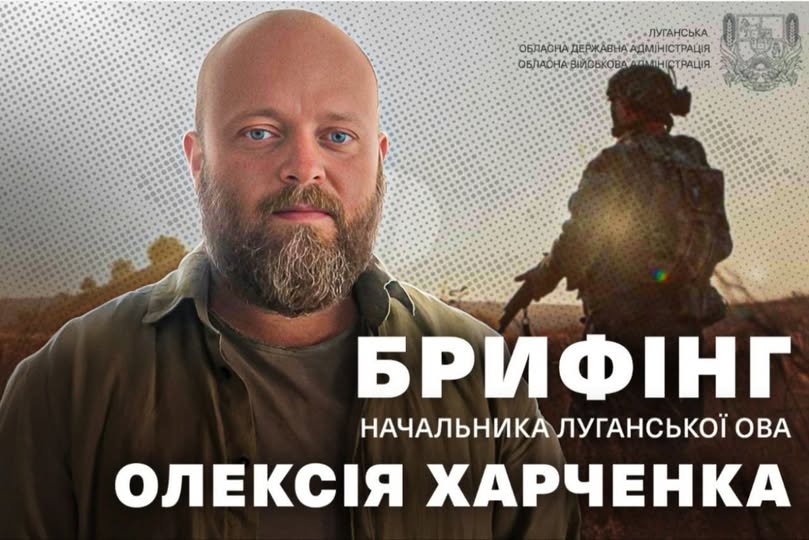 На інформаційному банері Луганської обласної державної адміністрації зображений портрет світлоокого бородатого чоловіка, Олексія Харченка, на фоні силуету військового у спорядженні та великого білого напису «БРИФІНГ НАЧАЛЬНИКА ЛУГАНСЬКОЇ ОВА», що анонсує офіційний виступ керівника області.