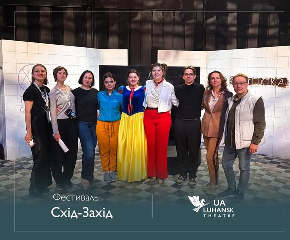 На фоні сценічних декорацій із білої плитки стоїть група з дев'яти людей, серед яких виділяється жінка в костюмі Білосніжки, а внизу розміщено написи «Фестиваль Схід-Захід» та емблему Луганського театру