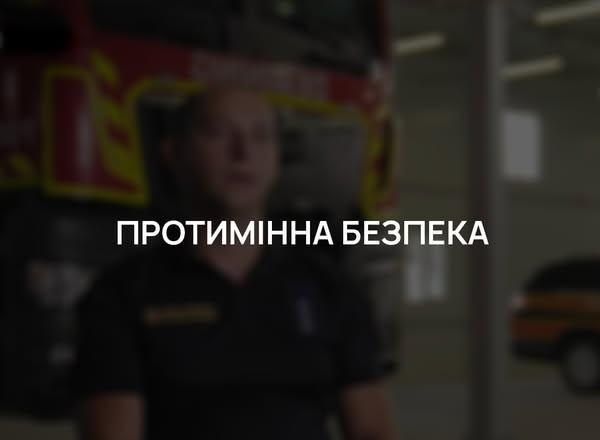 На затемненому фоні, де розмито видно чоловіка у формі рятувальника на фоні пожежної машини, по центру розміщено чіткий білий напис великими літерами «ПРОТИМІННА БЕЗПЕКА»