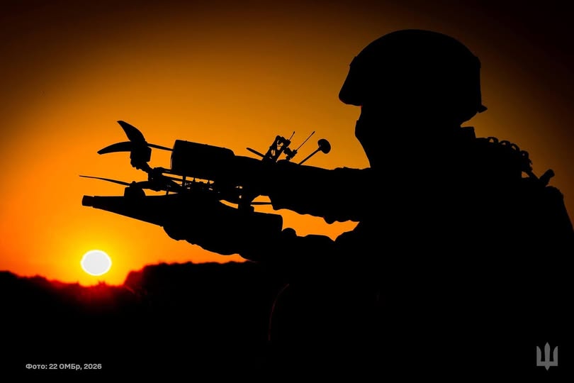 На світлині зображено темний силует українського військового в касці, який тримає в руках FPV-дрон-камікадзе з прикріпленим боєприпасом на тлі яскраво-оранжевого заходу сонця, з офіційним підписом «Фото: 22 ОМБр, 2026» ліворуч та військовим тризубом у нижньому правому куті