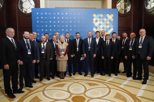 Група людей у ділових костюмах, серед яких одна жінка, стоїть на тлі синьо-жовтого банера під час офіційного заходу