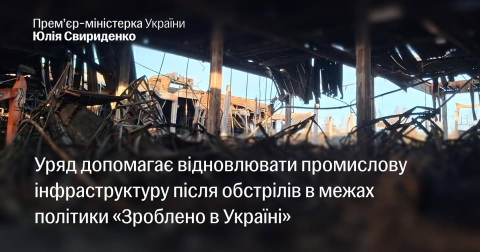 На інформаційному банері з цитатою про урядову допомогу у відновленні промислової інфраструктури в межах політики «Зроблено в Україні» зображено масштабні руйнування всередині виробничого або складського приміщення зі знищеним дахом та купою понівеченого металу після обстрілу