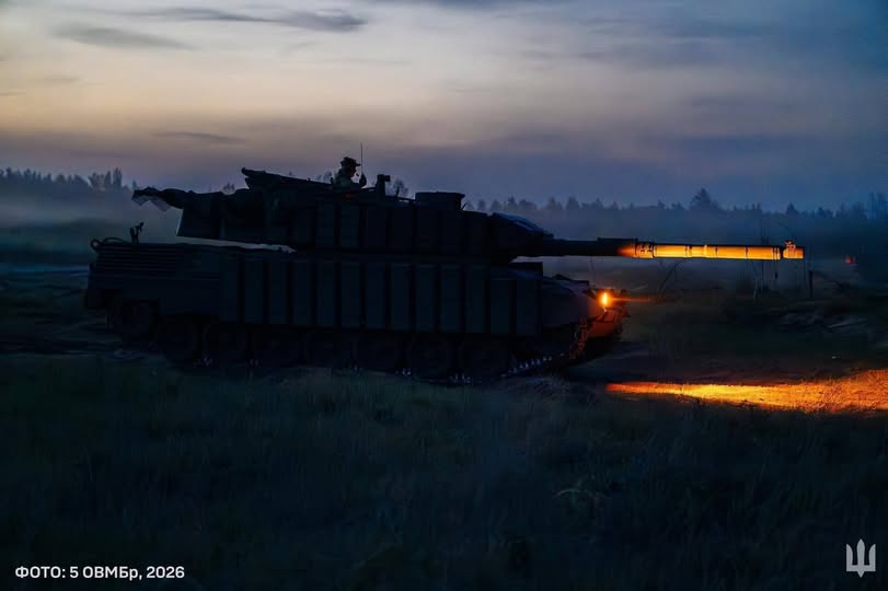 На фото зображено силует танка у сутінках на полі, ствол якого підсвічений яскравим помаранчевим світлом фар, а в лівому нижньому кутку міститься напис «ФОТО: 5 ОШБр, 2026»