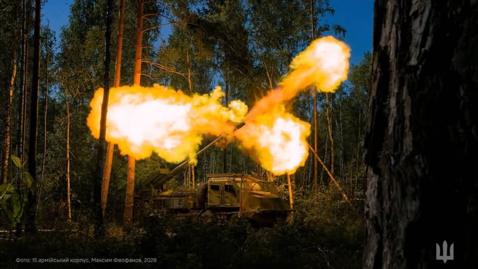 На фото зображено українську самохідну артилерійську установку в лісі вночі, з гармати якої в момент пострілу вириваються великі яскраві спалахи вогню та диму