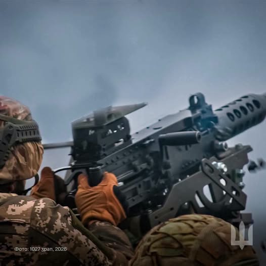 Український військовий у камуфляжній формі та шоломі цілиться з великого автоматичного кулемета на вертлюжній установці на тлі хмарного неба.