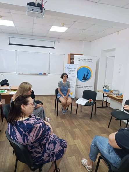 Група людей сидить на стільцях у колі під час зустрічі у світлому офісному приміщенні з білими дошками та банерами громадської організації «Десяте квітня» на задньому плані