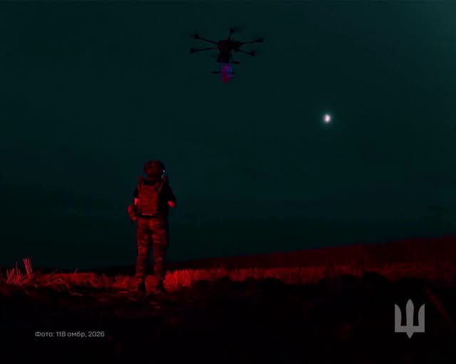 На нічній світлині зображено військовослужбовця у повному бойовому спорядженні, який стоїть спиною до глядача посеред темного поля.