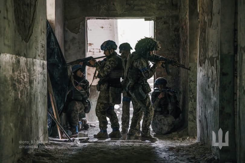 Група українських військових у повній бойовій екіпіровці зі зброєю в руках веде бій або тримає оборону всередині зруйнованої будівлі