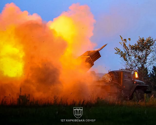 Військова реактивна система залпового вогню на базі вантажівки здійснює бойовий постріл у сутінках, утворюючи величезну вогняну хмару диму та полум'я.