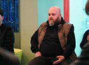 На фотографії крупним планом зображений чоловік середнього віку, який сидить у приміщенні.