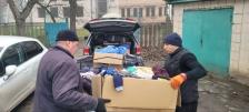 Двоє чоловіків перевантажують велику картонну коробку з одягом із багажника автомобіля
