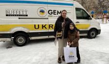 Жінка та дитина позують біля брендованого фургона гуманітарної допомоги від фондів The Howard G. Buffett Foundation та GEM Ukraine на засніженій вулиці.