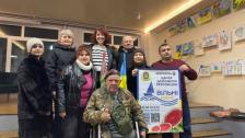 зображено легендарного українського волонтера Григорія Янченка, також відомого як дядько Гриша, який сидить в інвалідному візку в кімнаті з іншими людьми та банером «Центр допомоги херсонцям «Вільні разом», під час зустрічі з волонтерами в Кропивницькому