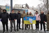 Група людей у зимовому одязі стоїть на вулиці в снігу, тримаючи банер із написом «ЛУГАНЩИНА» та картою області.