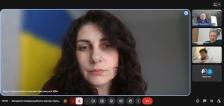 Скріншот відеоконференції. На головному екрані зображено жінку на тлі українського прапора, а праворуч — менші вікна інших учасників зустрічі