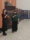 Зображення показує двох жінок, які стоять у приміщенні біля банерів із написами українською та англійською мовами, тримаючи мікрофони, що свідчить про проведення публічної події чи презентації.
