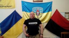 На цьому фото зображений чоловік міцної статури на фоні патріотичної символіки