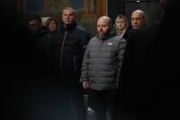 На цьому зображенні зафіксовано групу людей, які зосереджено за чимось спостерігають у приміщенні з приглушеним освітленням.