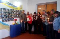 На цьому зображенні зафіксовано групу з дев’яти осіб (чоловіків та жінок), які зібралися в приміщенні, щоб вшанувати пам'ять загиблих захисників України