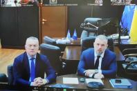 Скриншот онлайн-наради в Zoom за участю представників державної влади та місцевого самоврядування, де в центрі за робочим столом сидять двоє посадовців у костюмах