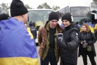 На фото зображені українські захисники та волонтери, які з усмішками роблять спільне селфі під час зустрічі після обміну полоненими на тлі автобусів
