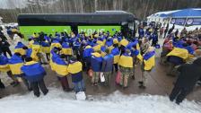 На фото зображено звільнених з полону українських захисників, які стоять біля автобуса, загорнуті в національні прапори України