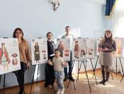 Четверо дорослих та дитина позують поруч із виставковими стендами, на яких представлені ілюстрації та описи традиційного українського вбрання