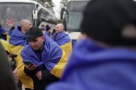 Українські військові, загорнуті в національні прапори, емоційно спілкуються телефоном та святкують своє повернення додому під час обміну полоненими біля автобусів