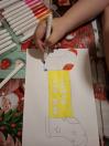  Дитяча рука синім фломастером розмальовує верхню частину зображеної на папері шкарпетки. Поруч лежить відкритий набір різнокольорових маркерів (рожеві, червоні, помаранчеві відтінки) та один білий ковпачок.