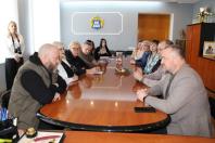 Робоча зустріч групи людей за великим овальним столом у конференц-залі. Учасники сидять один навпроти одного, ведучи активне обговорення. На центральній стіні розміщено герб міста Кропивницького.