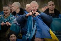 Група звільнених українських захисників та цивільних, які повернулися додому в межах масштабного обміну полоненими 11 квітня 2026 року, висловлюють свою радість і вдячність, причому один із чоловіків у центрі зворушливо складає руки у формі серця на тлі національних стягів.