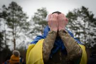 Український захисник, загорнутий у національний прапор, не стримує сильних емоцій і закриває обличчя руками після звільнення з тривалого російського полону під час масштабного обміну 11 квітня 2026 року на фоні похмурого весняного лісу.