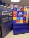 У приміщенні America House Kyiv поруч із синім стендом виставки «Реальність окупованого музею» розташована яскрава фотозона з логотипом закладу, кольоровими піктограмами, невеликими синіми сходами та гірляндою з прапорців США вгорі.